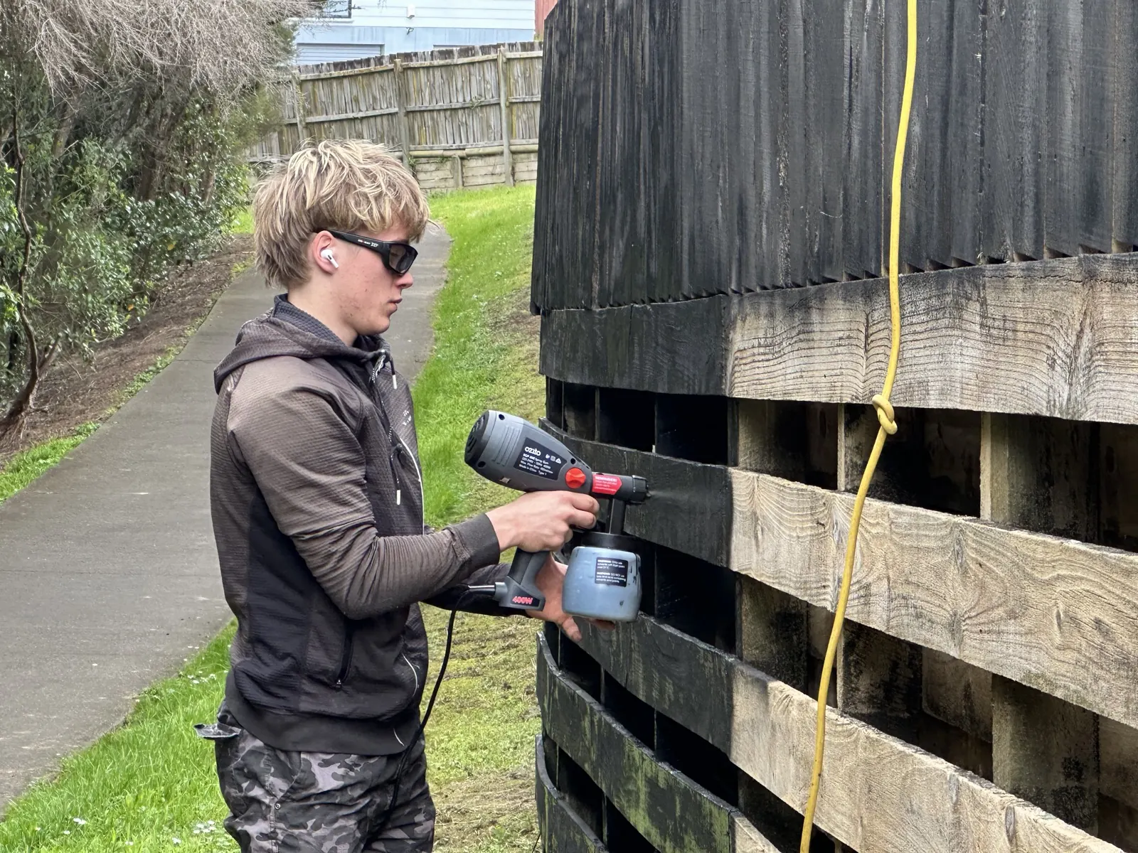 Spraying a timber boundary fence black with an electric spray gun in Sunnyhills, East Auckland