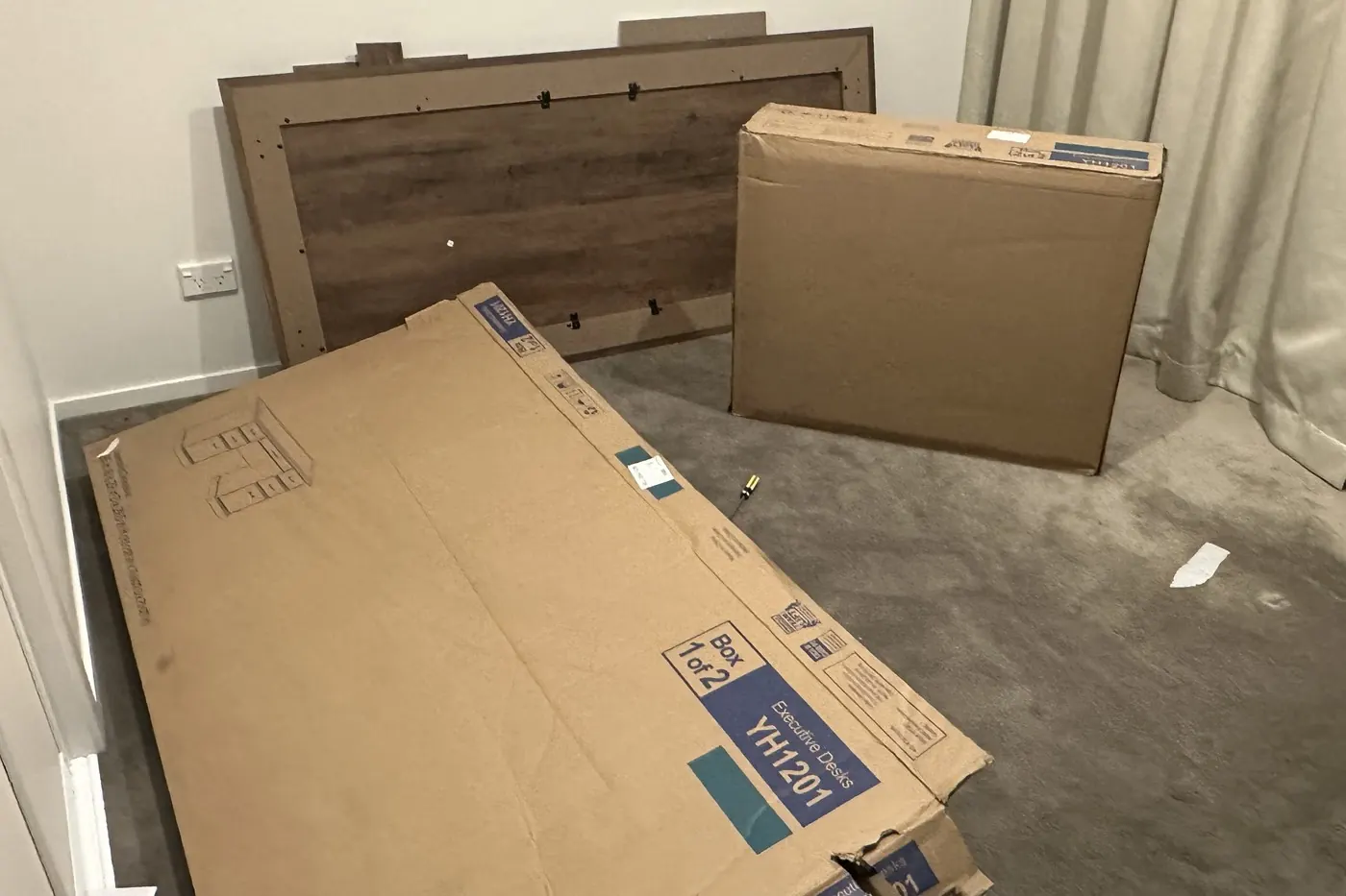 Two flat-pack boxes and a desk back panel on the bedroom floor in Parnell, before assembly