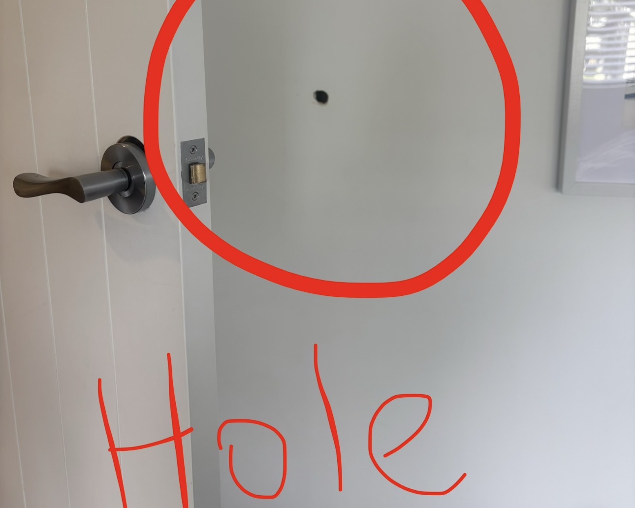 Small hole in the plasterboard wall beside a door in Mellons Bay, ringed in red so it can be seen