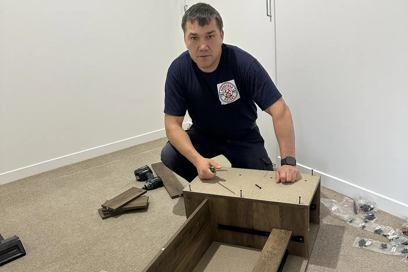 Desk panels, drawer runners and bagged fixings laid out on the carpet in Flat Bush, part-way through assembly