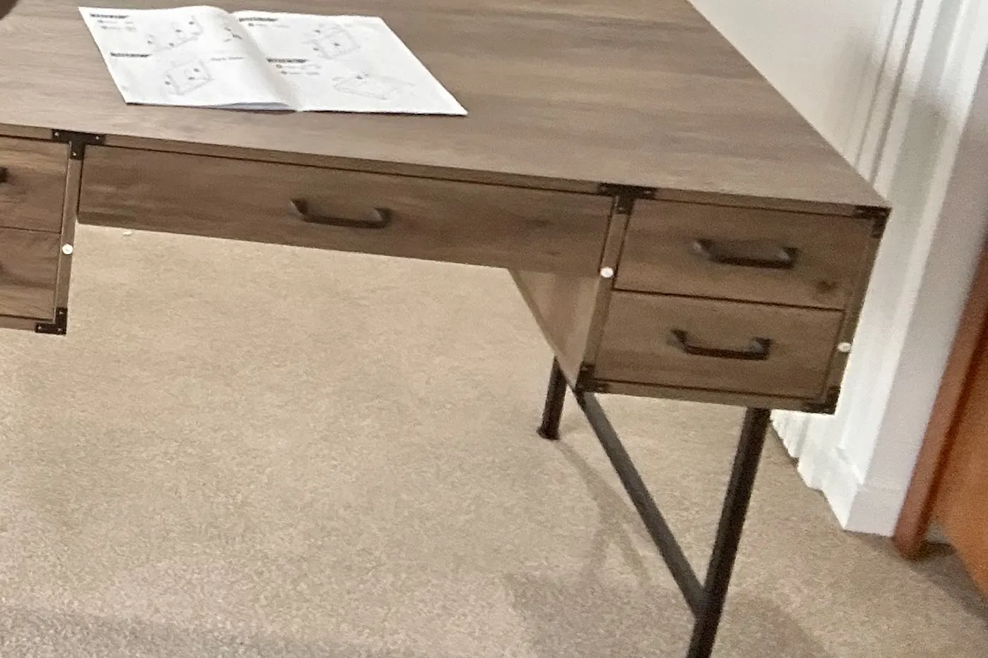 The finished desk standing on its steel legs in the same Flat Bush room, drawers fitted and instructions still on the top