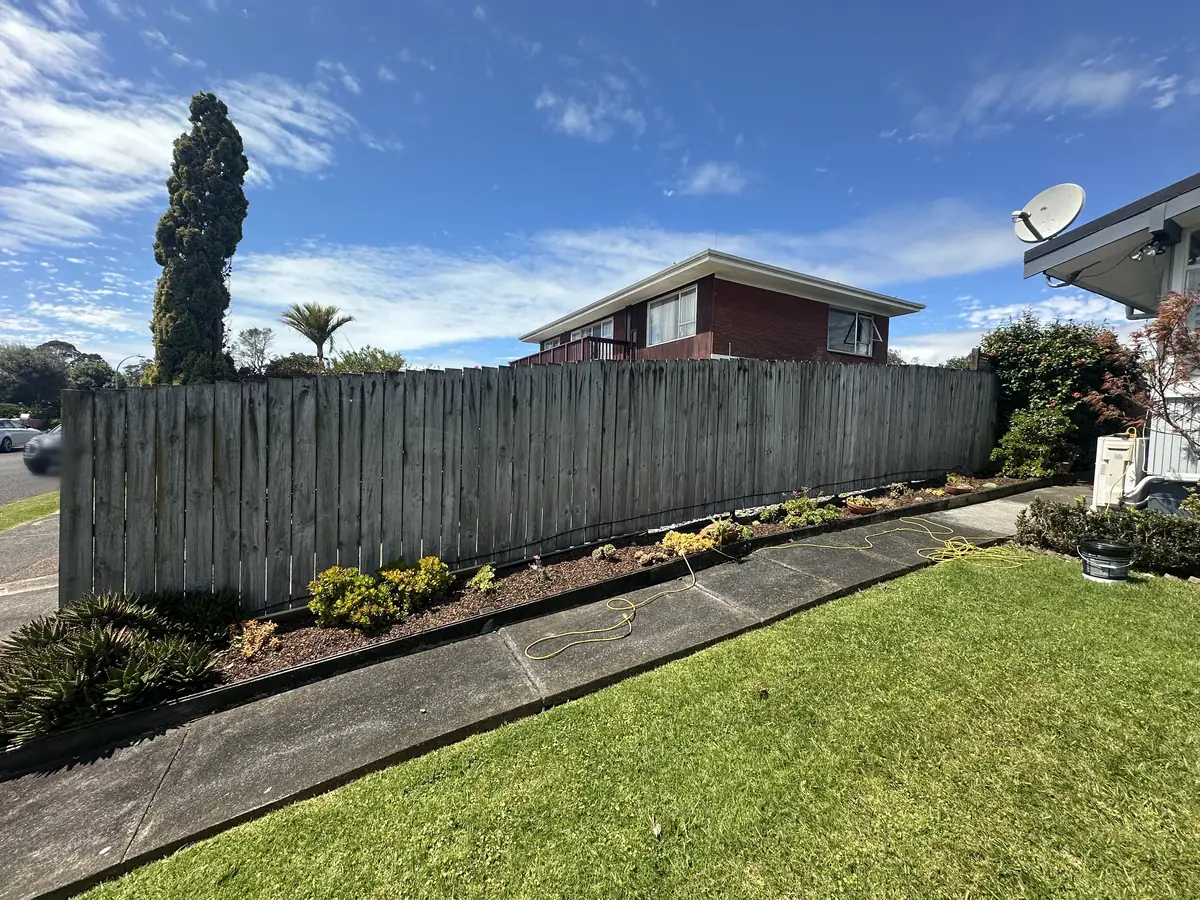 Long timber paling fence in Pakuranga Heights before painting, weathered to a patchy silver grey, with a planted garden strip running along the base