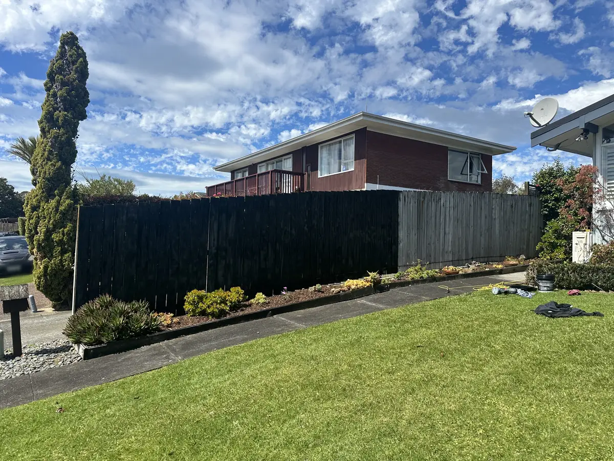 The same Pakuranga Heights fence part way through spray painting, with the near section finished black and the far section still weathered grey