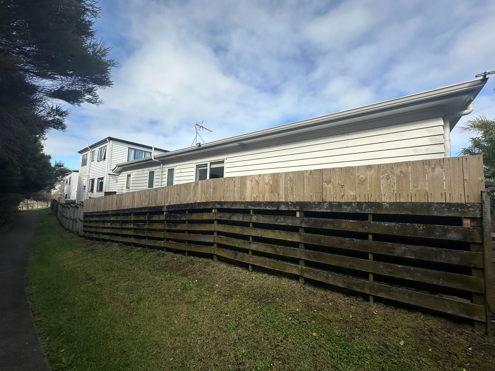 Timber boundary fence in Sunnyhills before work, with new lighter palings added on top of the old dark rails
