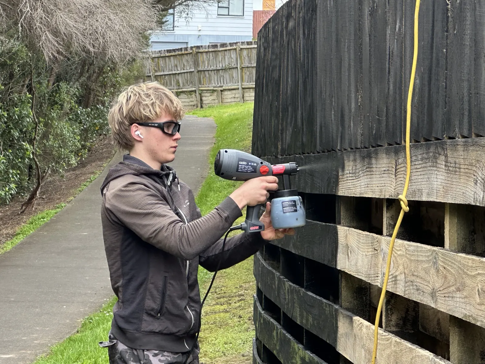 An apprentice spraying black paint onto the fence with an electric spray gun
