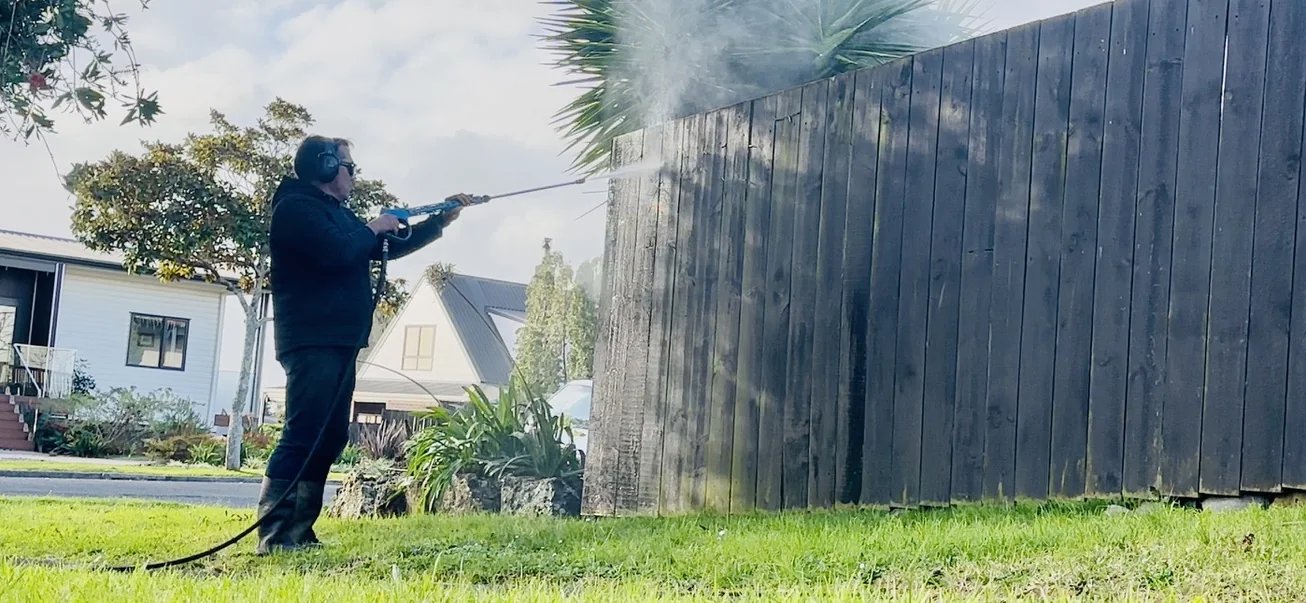 Rinat using a water blaster to clean moss from a timber fence in Highland Park