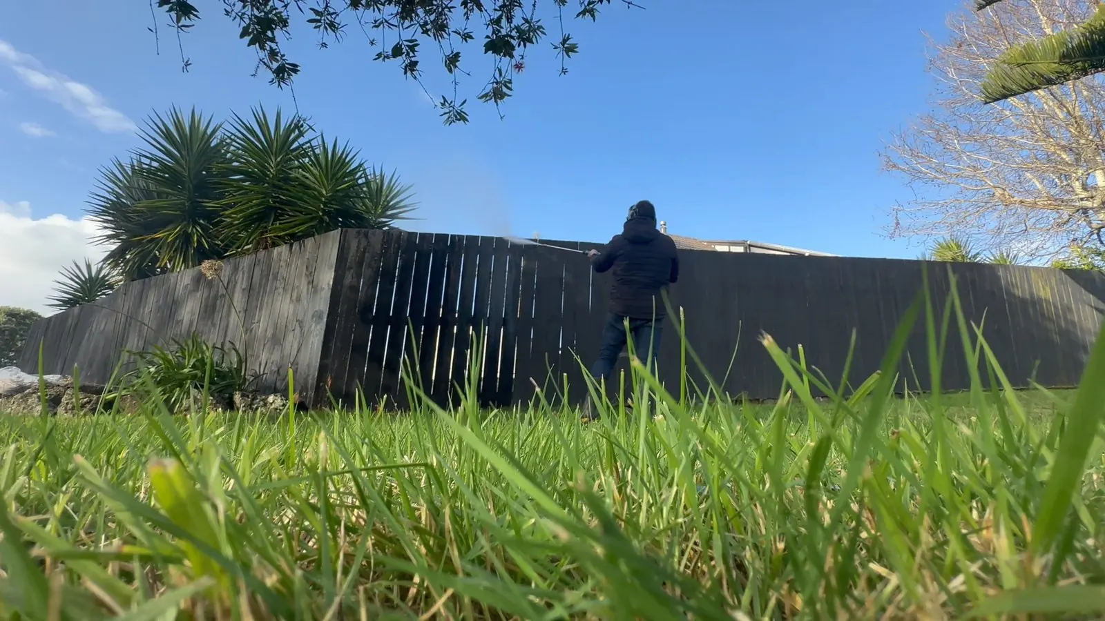 Low-angle view of water blasting in progress on an uneven black timber fence in Highland Park