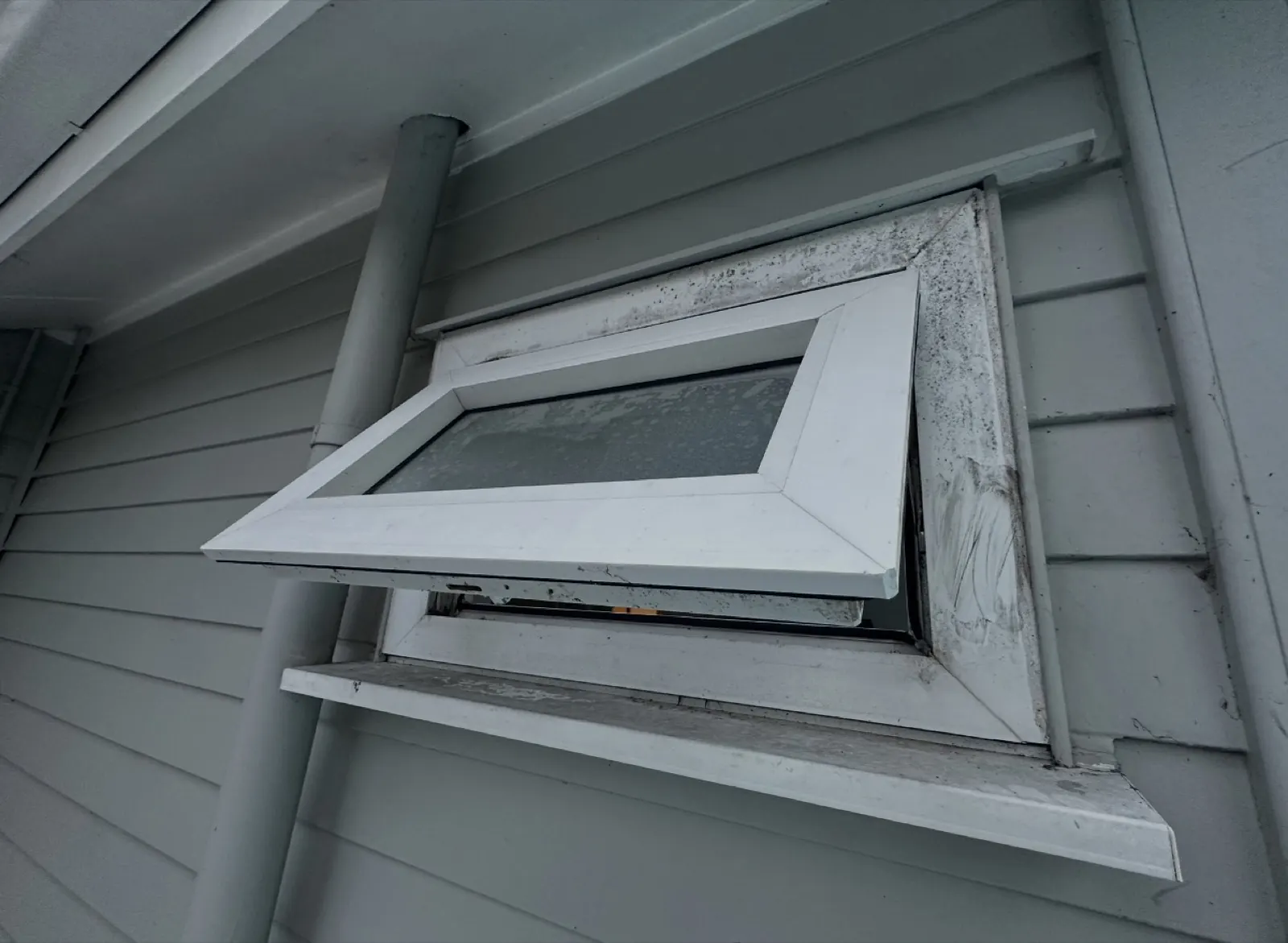 The PVC sash hanging open and out of line from outside the house, no longer held square by its stays