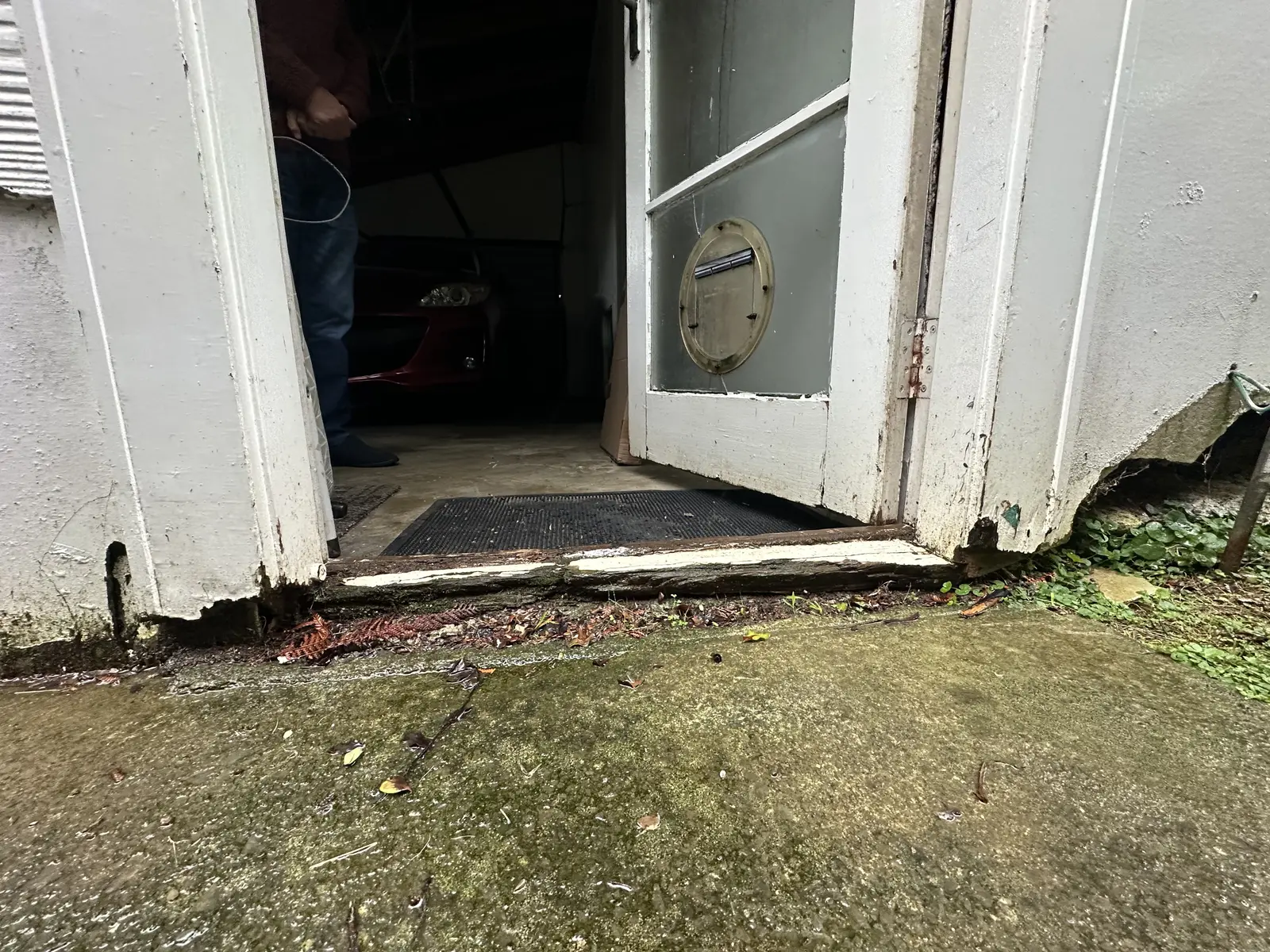 Rotten timber door threshold with crumbling wood and moss at a garage entrance in East Tamaki, East Auckland