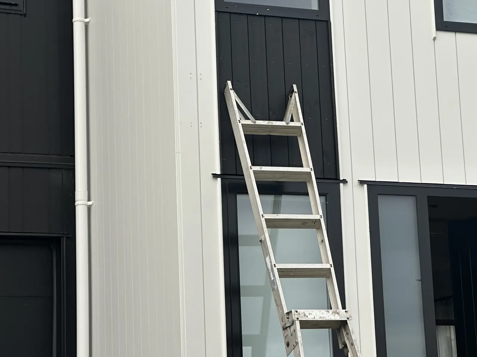 Ladder set up against the weatherboard wall of a Sunnyhills house to reach the camera positions above the door