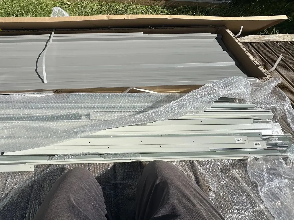 Metal garden shed panels and frame parts being unpacked from a flat-pack box