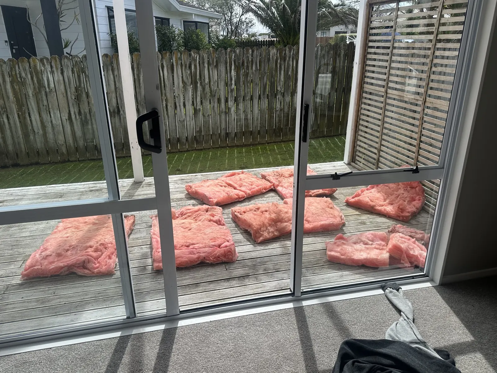 Pink insulation batts laid out to dry on a timber deck outside the Highland Park house