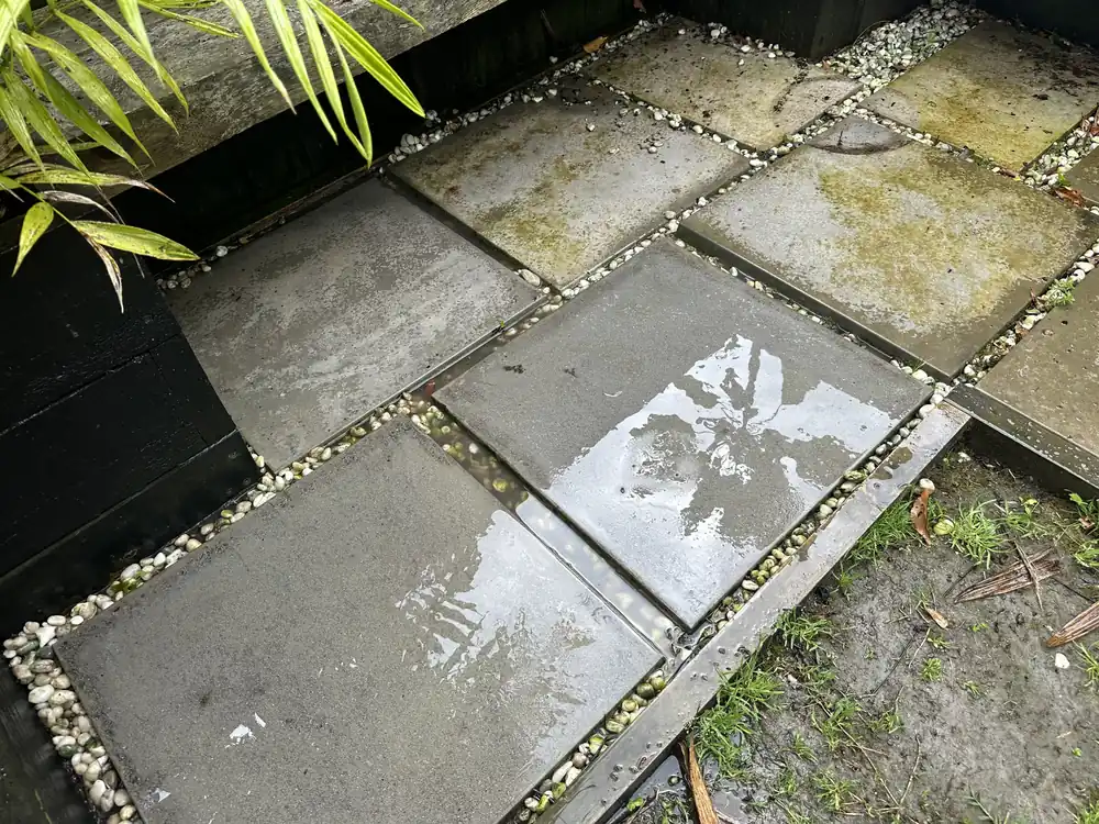 Pavers in the Pakuranga seating corner part way through water blasting, with clean stone appearing against the mossy sections