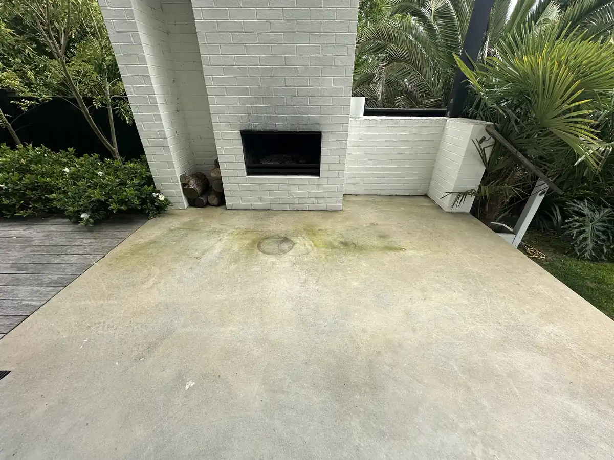 Concrete BBQ area in front of a white brick outdoor fireplace in Pakuranga before cleaning, stained green with moss and marked with old paint